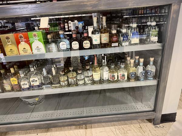 Glass counter case with top-shelf tequila, including Patrón gift boxes, Don Julio and 1800