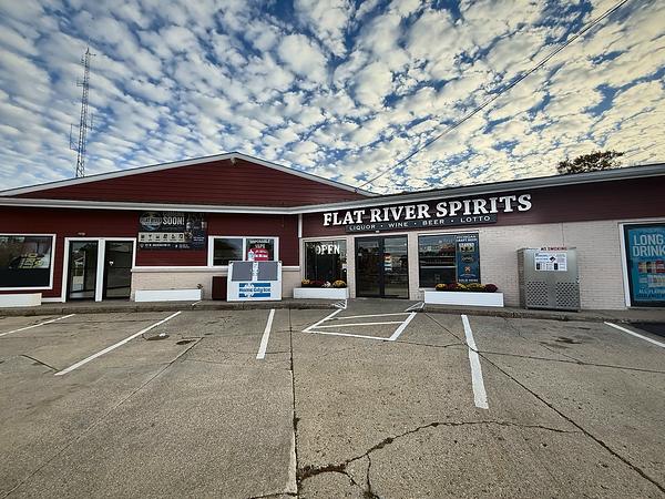 Flat River Spirits storefront and parking lot on W Washington St under a blue, cloudy sky