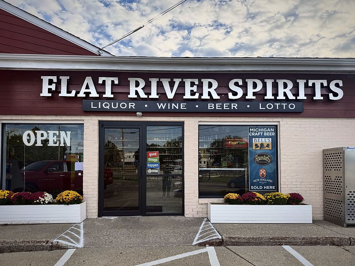 The Flat River Spirits storefront on W Washington St, with a sign reading Liquor, Wine, Beer, Lotto above the front doors and flower planters under the windows